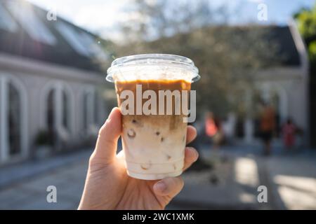 Hand holding iced latte in plastic glass on outside garden at coffee shop in bright day Stock Photo