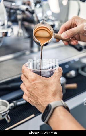 Barista pouring espresso coffee from dosing cup to plastic cup in coffee shop Stock Photo