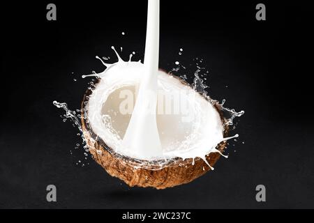 Coconut cut in half with milk splash isolated on black stone background Stock Photo