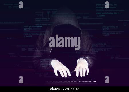 Cybercriminal in a hood without a face sits in the dark behind a laptop on dark background Stock Photo