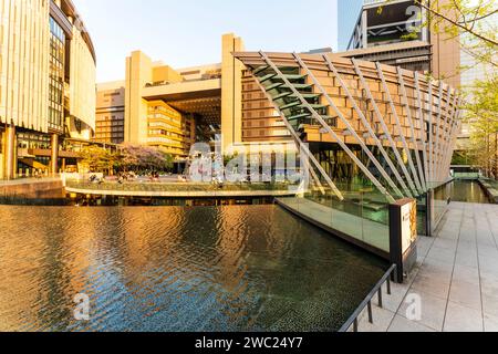 Umekita Ship Hall and water feature with the North gate building of Osaka Station city behind, lit up by the setting sun (unseen), in the springtime. Stock Photo