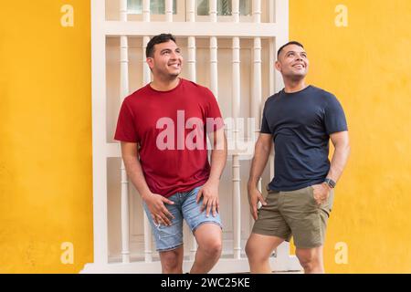 Two smiling men in casual attire lean on an ornate balcony, enjoying urban life. Stock Photo