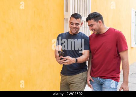 Two men share a laugh while looking at a smartphone together. Stock Photo