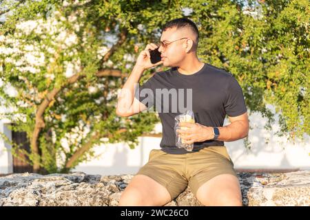 Latin Man Multitasking with Phone Call and Snack Outdoors Stock Photo