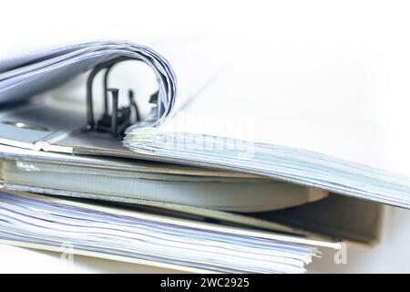 Part of an open ring binder with many documents on a stack of more file folders, business and office concept fading to a white background, copy space, Stock Photo
