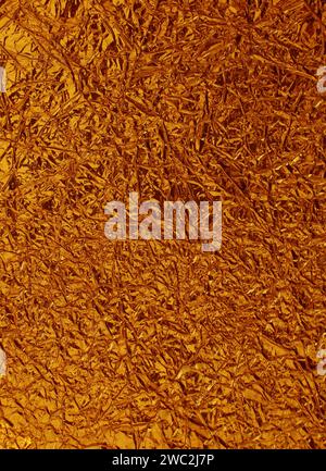 Gold crumpled foil surface. Abstract background from red-yellow silvery foil close-up. Stock Photo