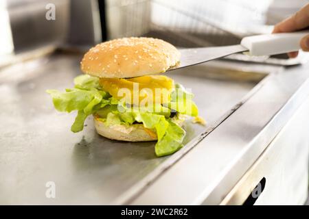 cooking, assembling a burger with bread, cheese, meat and lettuce, in fast food restaurant, fresh ingredients, studio photo at workplace Stock Photo