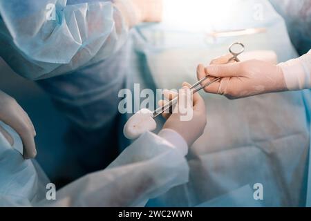 Closeup top view of unrecognizable African nurse assists surgeons, giving surgical clamp with tampon during surgical operation. Stock Photo