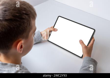 Boy at work desk, close-up view from behind, interacting with a tablet's isolated screen for game or app promotion. Engaged in digital entertainment Stock Photo