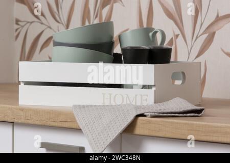 Ceramic bowls and mugs in the wooden box on the kitchen counter, domestic life organization concept Stock Photo