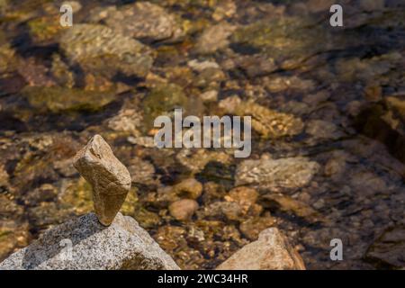 Large rock shaped like a thumb balanced on top of another larger stone at edge of shallow river Stock Photo