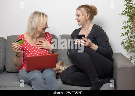 Laughing mother a  daughter shopping from home using laptop and smartphone. Horizontally. Stock Photo