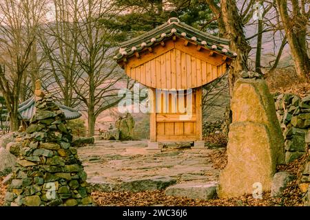 Small wooden oriental building with tiled roof in front of rock wall at countryside roadside park on winter evening Stock Photo