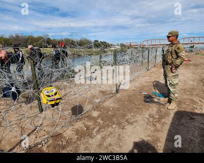 Eagle Pass, United States. 19 December, 2023. Texas Army National Guardsmen watch as migrants crossing the Rio Grande encounter razor wire blocking access at the Texas-Mexico border, December 19, 2023 in Eagle Pass, Texas. The soldiers are acting on orders from the Texas Governor as part of the state sponsored Operation Lone Star.  Credit: 1SG Suzanne Ringle/Texas National Guard/Alamy Live News Stock Photo