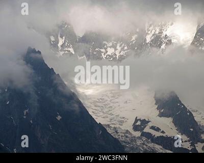 Atmospheric view of the Italian Alps above Courmayeur with weak sunshine piercing the low clouds over the snowy peaks and crags Stock Photo