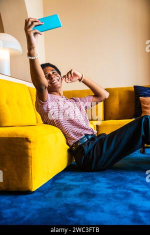 Fluid gender young man wearing cross dressing clothing at home, LGBTQ and diversity concepts - Hispanic non binary male portrait in a colorful apartme Stock Photo