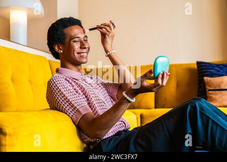 Fluid gender young man wearing cross dressing clothing at home, LGBTQ and diversity concepts - Hispanic non binary male portrait in a colorful apartme Stock Photo
