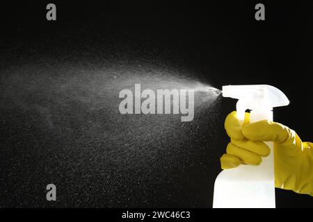 Woman spraying liquid from bottle on black background, closeup Stock Photo