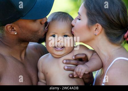Mothers and father kissed Biracial baby. kissing baby. Mother kiss child, father caring baby. Closeup face of multiracial couple kissing Biracial baby Stock Photo