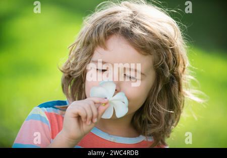 Funny child smelling plumeria flower, face close up. Kids in summer nature park, portrait. Stock Photo