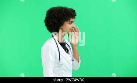 Female doctor, close-up, on a green background, tells a secret Stock Photo