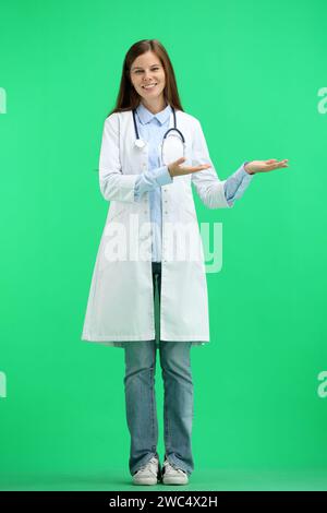 A full-length female doctor, on a green background, points to the side Stock Photo