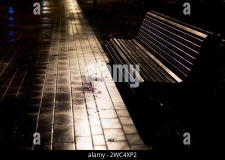 a bench and a wet road in a night park without lanterns. Benches in the park in autumn, at night Stock Photo