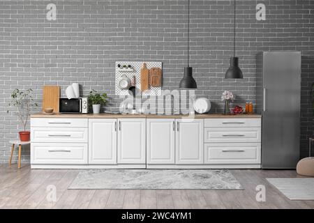 Interior of modern kitchen with white counters and pegboard hanging on grey brick wall Stock Photo