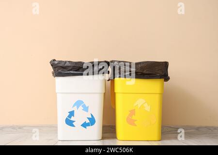 Empty trash bins with garbage bag and recycle logo near beige wall Stock Photo