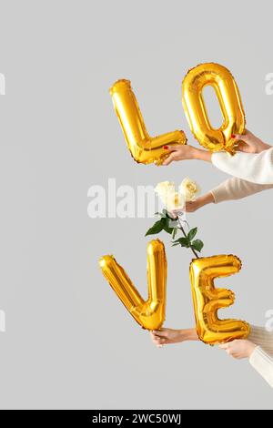 Female hands holding word LOVE made from balloons and roses on white background. Valentine's Day celebration Stock Photo