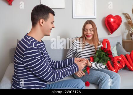 Young man putting engagement ring on his woman's finger at home on Valentine's Day Stock Photo