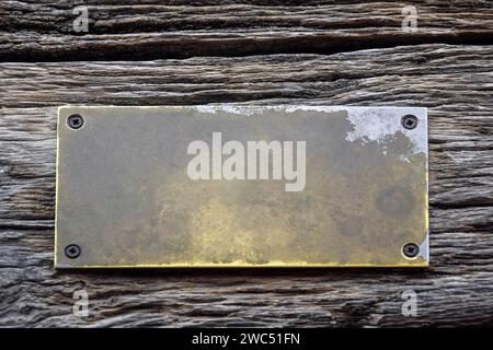 Antique blank brass rectangular plaque screwed with rusty screws to an old weathered board with deep wrinkles. Place for text on bronze plate. Copy sp Stock Photo