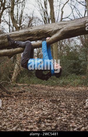 A woman fools around hanging upside down on a fallen tree in the woods Stock Photo