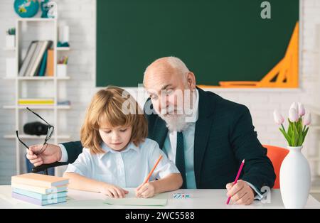 Old teacher and young schoolboy doing homework assignment at school. Teachers day. Stock Photo