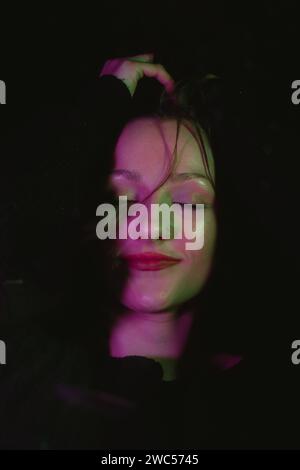 A captivating image featuring a serene woman with closed eyes, radiating an ethereal glow in a dimly lit room Stock Photo