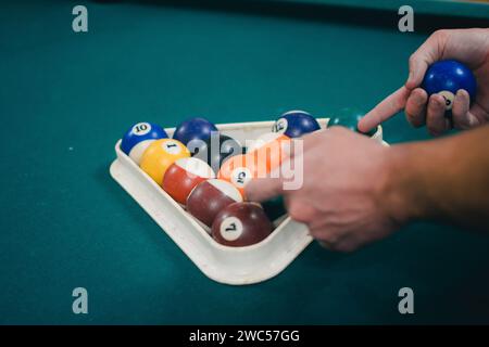This image showcases a close-up view of a person's hands carefully selecting billiard balls from a tray placed on a vibrant pool table Stock Photo