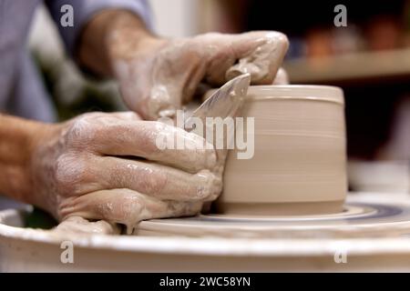 male hands making ceramic cup on pottery wheel with special wooden tool, Close-up Stock Photo