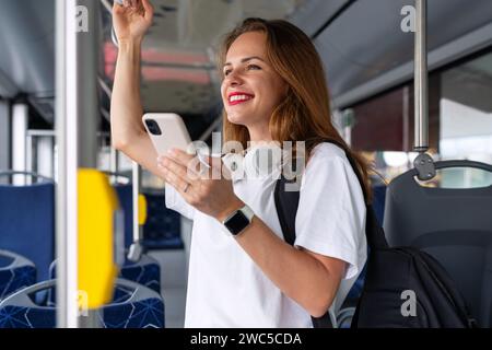 Attractive brunette woman with red lips using her smart phone while traveling by city bus. Stock Photo