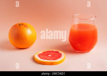 Grapefruit next to a slice and a glass with its orange-red juice on a pink background. Stock Photo