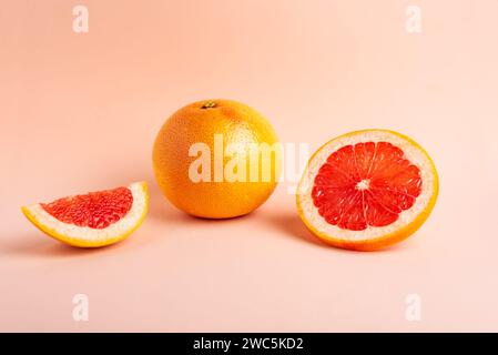 Grapefruit next to a slice and a piece on a pink background. Stock Photo