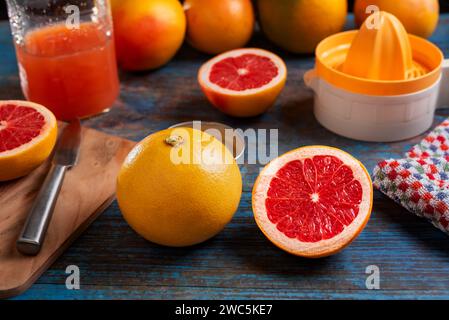 Grapefruits, some opened in half next to a cutting board, a jug with juice and a manual juicer. Stock Photo