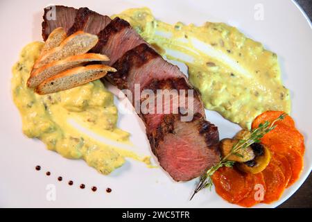 Steak medium roast, cut into pieces in creamy mushroom sauce. Steak served on a white plate and wooden table. Stock Photo