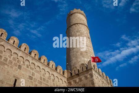 Looking up at the  imposing walls, ramparts and tower of the 8th century religious fortress, the Ribat of Sousse with a Tunisian flag flying in Tunisi Stock Photo