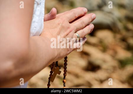 Christian woman praying in front of cathedral. Hands of pilgrim holding the rosary. Woman with hands crossed. Stock Photo