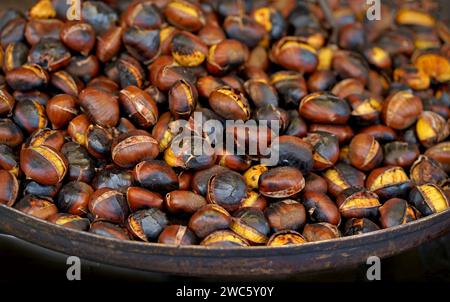 Fried chestnuts in a pan on a wooden stand, flat lay. Fresh roasted chestnuts for christmas or holidays Stock Photo
