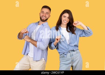 Joyful couple dancing and smiling in denim on yellow background Stock Photo