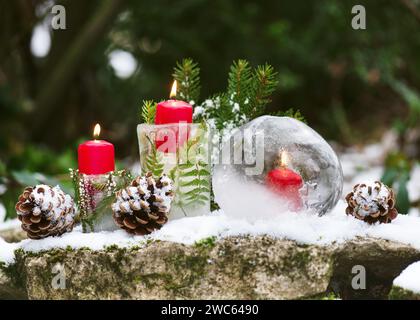 Beautiful floristic arrangement with  ice lantern and candles in the evening in the snow covered garen. Winter craft and Ice art or outdoor decoration Stock Photo