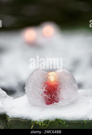 Ice globe lantern with red candle burning inside in the evening garden. Winter craft and Ice art or outdoor decoration concept. Stock Photo