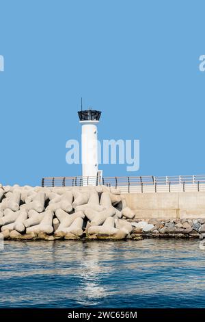 White lighthouse on concrete pier against clear blue sky Stock Photo