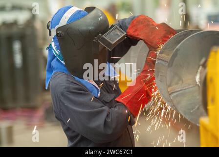 Industrial worker using an angle grinder at the early stages of making a screw conveyor from carbon steel.. Stock Photo